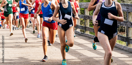 High school girls cross country race going over wood bridge