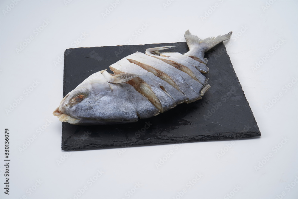 The dried pomfret is striped on the surface with a knife and placed on a plate against a white background The dried pomfret is striped on the surface with a knife and placed on a plate against a white background