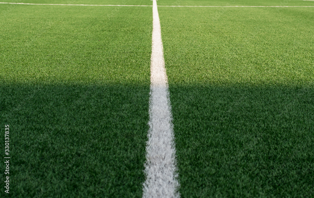 Artificial green grass and white border lines. Artificial turf for soccer field. Football field in an outdoor stadium. White lines on the road. Selective focus