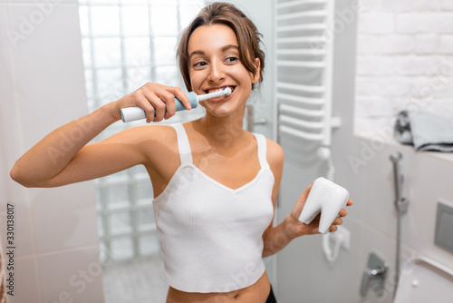 Принти на полотні Young and cheerful woman brushing teeth with electric toothbrush during morning