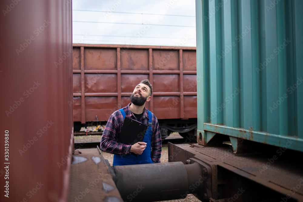 Railwayman checking train trailers before departure. Worker inspecting cargo shipping containers.