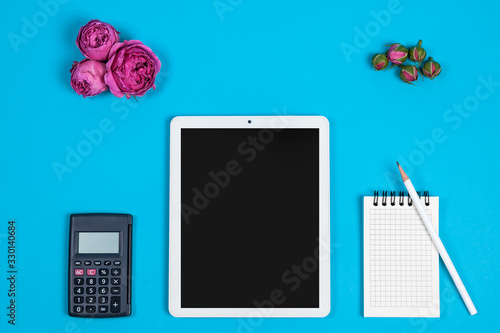 Fototapeta Naklejka Na Ścianę i Meble -  top view of the workspace on a blue background. calculator, Notepad, pencil, screen and pink flower buds