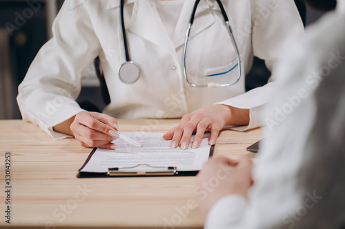 Cropped photo of female physician interviewing a patient and filling in medical documents