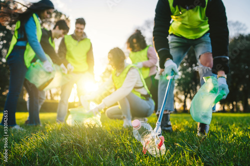 Group of friends during a volunteer garbage collection event in a park at sunset - Millennial having fun together - Happy people cleaning area with bags - Ecology concept photo