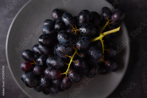 a cluster of juicy black grapes lies in a gray plate on a dark gray table