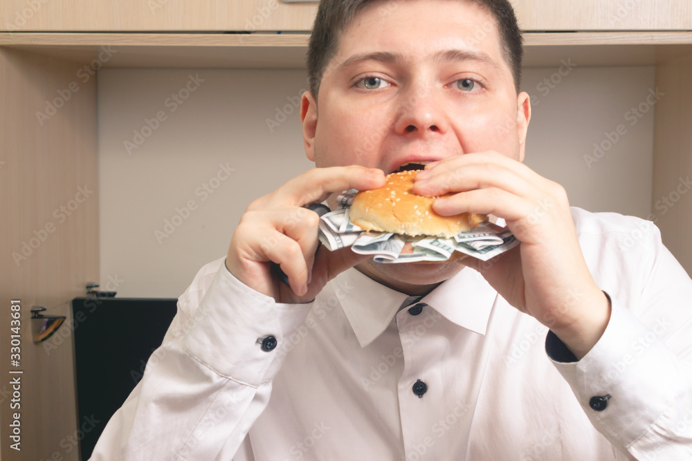 Caucasian man eating a burger with hundred dollar bills in a white shirt in the office Caucasian man eating a burger with hundred dollar bills in a white shirt in the office