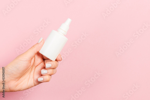 A bottle of nasal spray in a female hand at pink background with empty space for your design