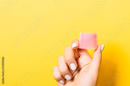 Close up of cosmetics jar in female hand at yellow background with copy space