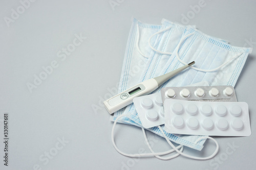 Pile of pills in blister packs, medical thermometer and mask on gray background. Disease prevention and treatment concept. Top view with free space for text. 