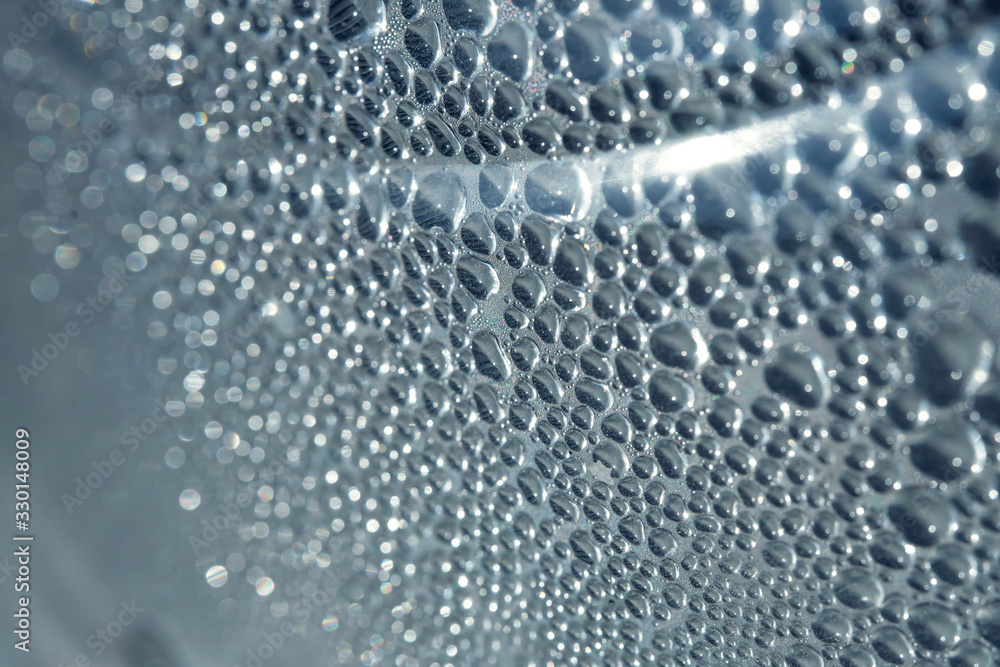 Fototapeta premium Drops of water close-up. The texture of the drops. Drops on the surface of a plastic bottle. Drawing of a drop of different sizes. Abstract blue background made of drops