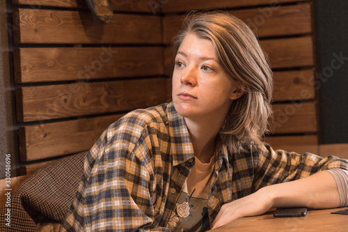 Blonde in a plaid shirt in a cafe, a mobile phone lies on the table.