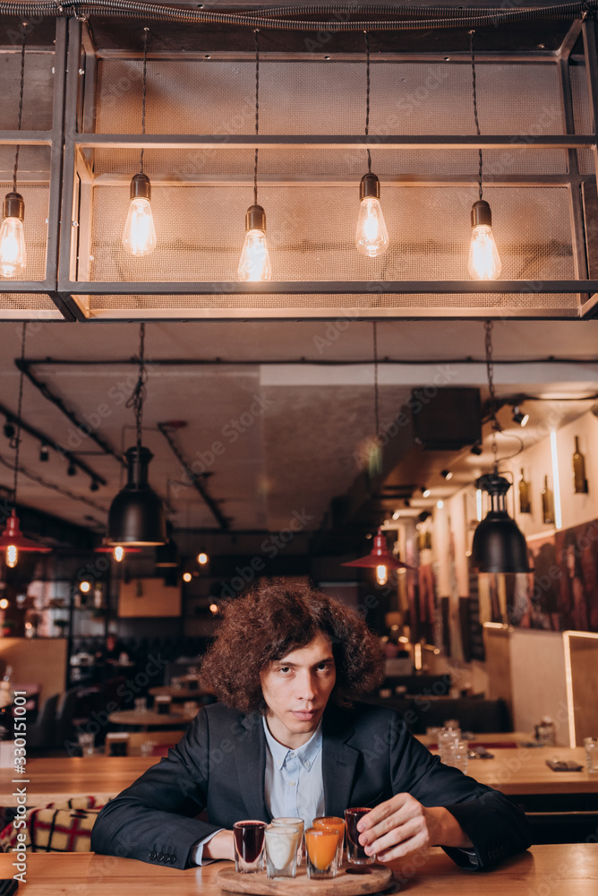 young curly-haired guy in a black suit drinking a liqueur in the bar