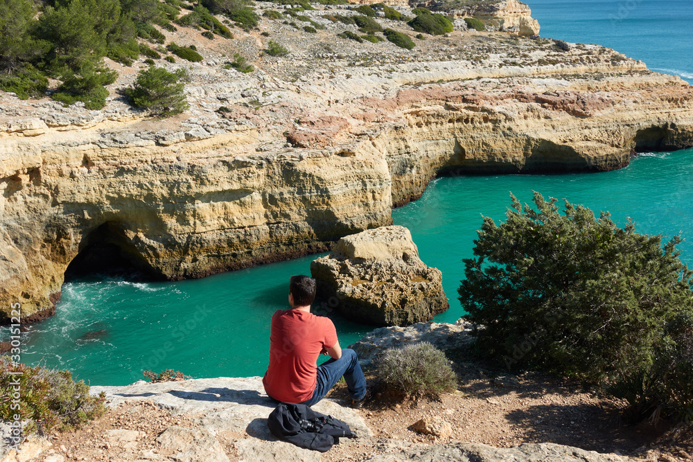 Man looking at a wild hidden secret beach with amazing turquoise water in Algarve, Portugal