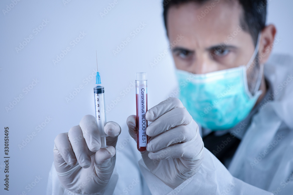 Medico con mascherina verde tiene in mano una provetta di sangue per il test del corona virus e una siringa Medico con mascherina verde tiene in mano una provetta di sangue per il test del corona virus e una siringa