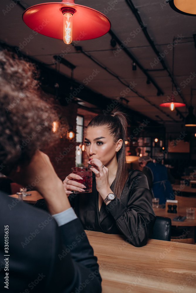 a young guy with curly hair and a beautiful girl in a dark dress with a glass of wine together in a restaurant a young guy with curly hair and a beautiful girl in a dark dress with a glass of wine together in a restaurant