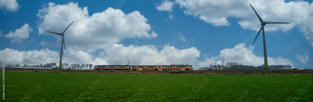 Panoramic dutch landscape with passenger train and two wind turbines