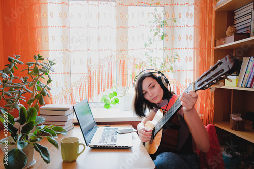 Female self education online. Woman plays guitar at front of laptop