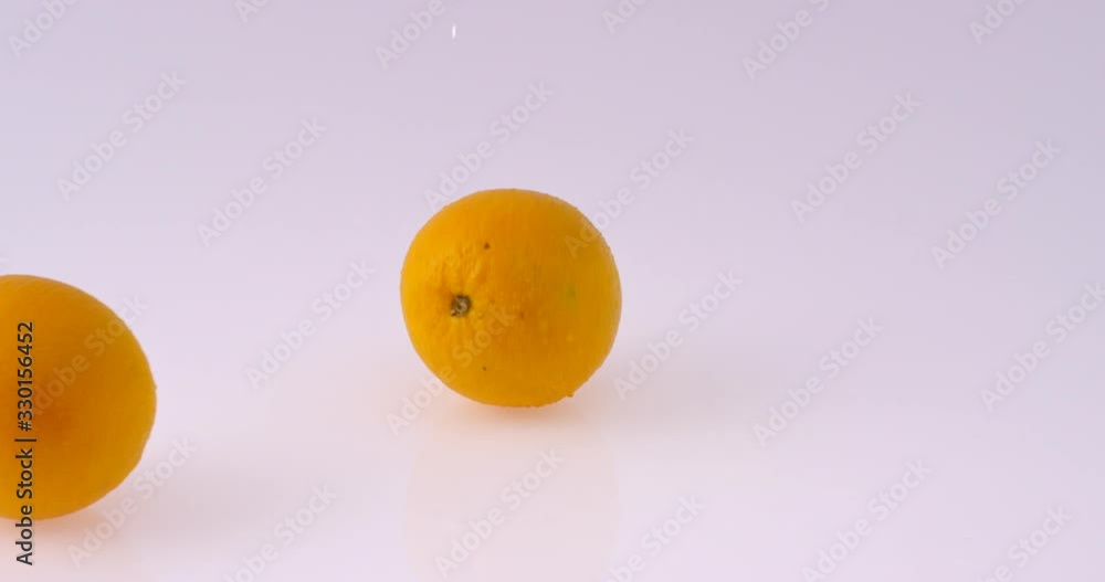Round Oranges (fruits) bouncing in ultra slow motion on reflective white background with water splashing Round Oranges (fruits) bouncing in ultra slow motion on reflective white background with water splashing