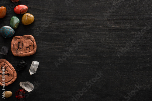 Top view of fortune telling stones, clay amulets and crystals on black wooden background