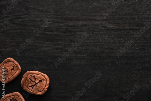 Top view of clay amulets with symbols on black wooden background with copy space