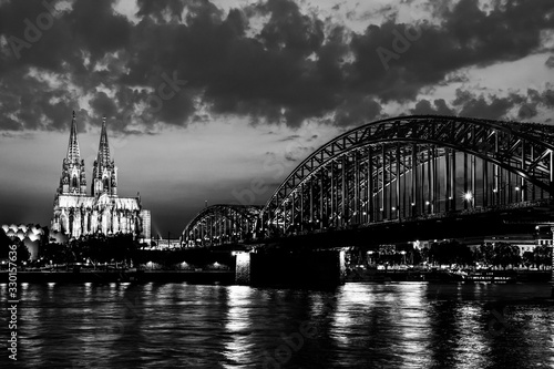 Beautiful black and white night landscape of the Cologne, Germany with gothic cathedral, railway and pedestrian Hohenzollern Bridge and reflections over the River Rhine