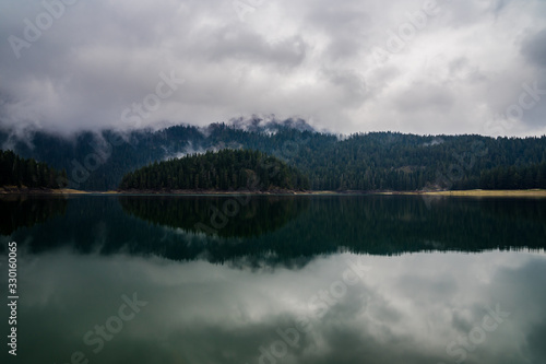 Montenegro, Glassy water of black lake in durmitor national park on foggy summer evening after rain in mystic atmosphere reflecting perfect forest nature landscape