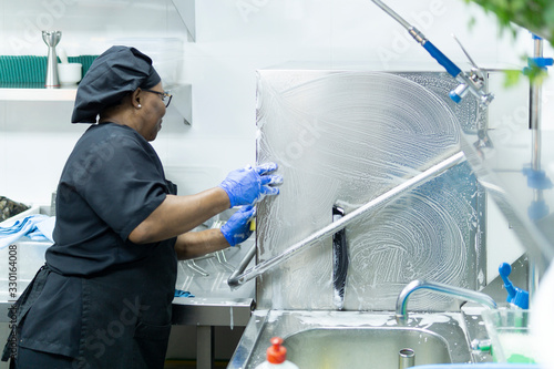 coronavirus. female chef disinfecting hospital kitchen in black uniform and blue latex gloves