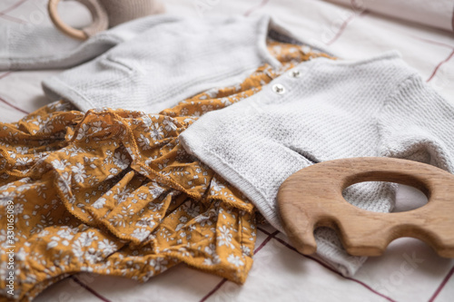 Mustard baby romper with knitted sweater and accessories with wooden toy and sunglasses.