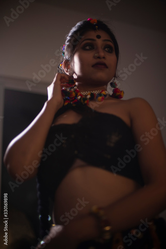 Low angle portrait of Indian Bengali brunette woman in Indian traditional tribal/ villager dress and handmade ornaments in dark studio background. Indian lifestyle and fashion photography.