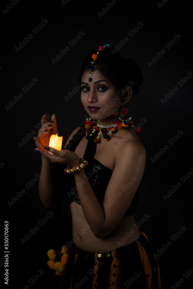 Portrait of Indian Bengali brunette woman in Indian traditional tribal/ villager dress and handmade ornaments with candle in dark copy space studio background.Indian lifestyle and fashion photography. Portrait of Indian Bengali brunette woman in Indian traditional tribal/ villager dress and handmade ornaments with candle in dark copy space studio background.Indian lifestyle and fashion photography.