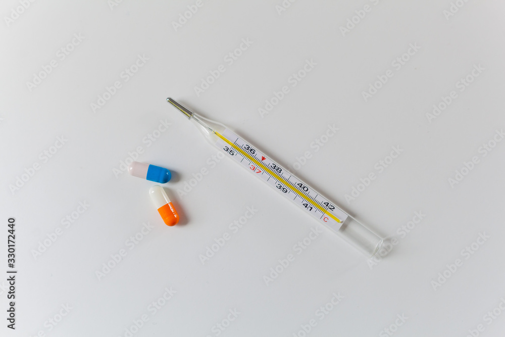 Thermometer and two capsules of orange and blue on a white table