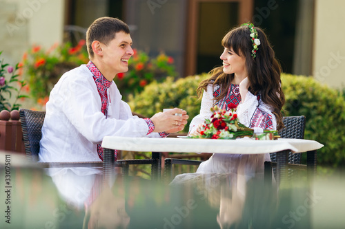 newlyweds in embroidered clothes in cafe drinking hot coffee and