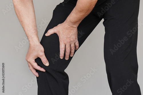 Hand of old male leg with painful kneeson isolated on a gray background. Elderly man feeling joint pain, having health issues and touching leg with hands. Health care concept.