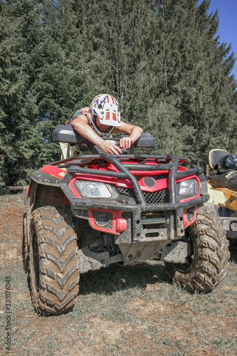 A young woman in a helmet for security configures the action camera on the hood of the red ATV in the background of the trees