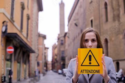 Coronavirus. Girl holds a yellow sign in her hands with the text Atenzione in Italian. The concept of pandemic and infectious diseases worldwide. Girl on the street of Italy in the city of Bologna.  photo