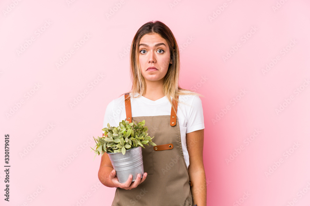 Young caucasian gardener woman in a pink background shrugs shoulders and open eyes confused. Young caucasian gardener woman in a pink background shrugs shoulders and open eyes confused.