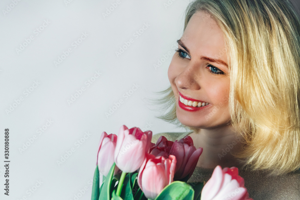 portrait of a beautiful girl with fresh flowers smiling on a light background. a young blonde woman in light clothing looks to the left, copy space