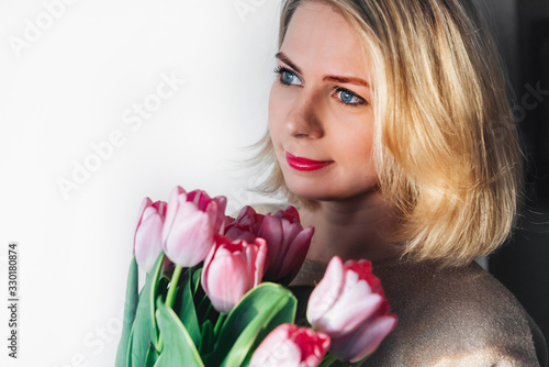 portrait of a beautiful girl with fresh flowers on a light background. a young blonde woman in light clothing looks to the left, copy space