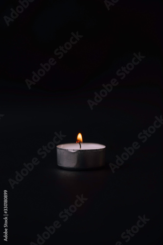 Stock photo of lit small white candle on black background.