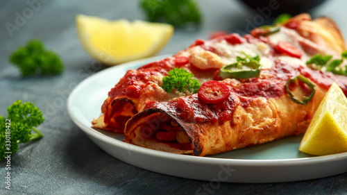 Baked Chicken fillets enchiladas with courgette, salsa sauce and cheese served with lemon wedges and chilies