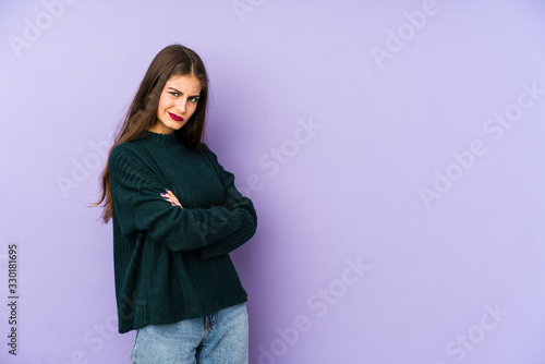 Young caucasian woman isolated on purple background frowning face in displeasure, keeps arms folded. © Asier