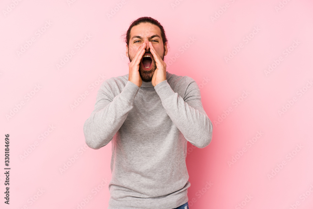 Young long hair man isolated on a pink background shouting excited to front. Young long hair man isolated on a pink background shouting excited to front.