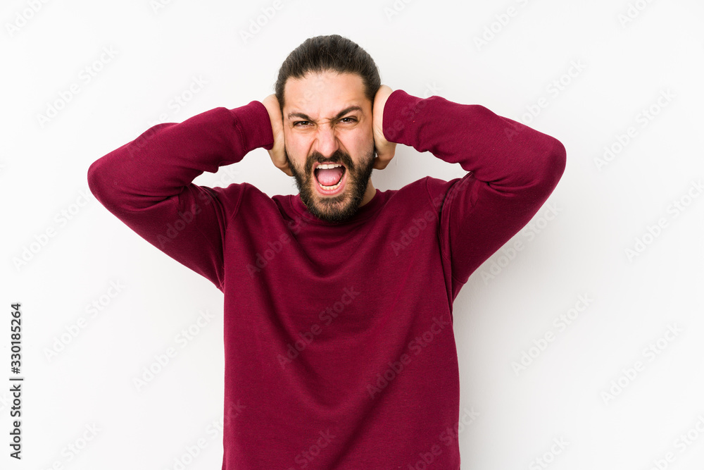 Young long hair man isolated on a white background covering ears with hands trying not to hear too loud sound. Young long hair man isolated on a white background covering ears with hands trying not to hear too loud sound.