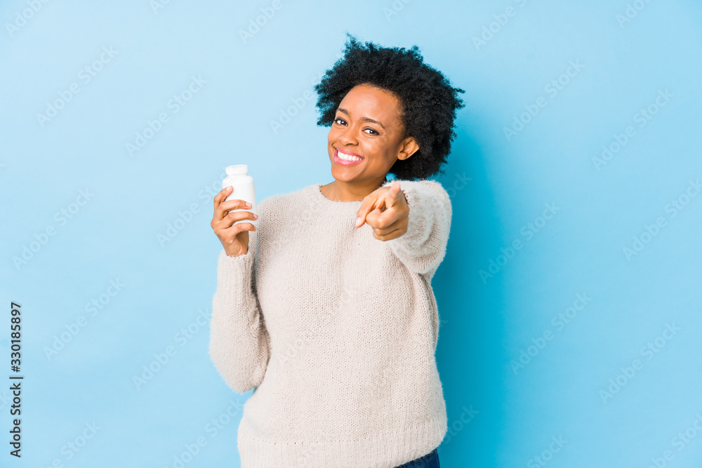 Middle age african american woman holding a vitamin bottle cheerful smiles pointing to front. Middle age african american woman holding a vitamin bottle cheerful smiles pointing to front.