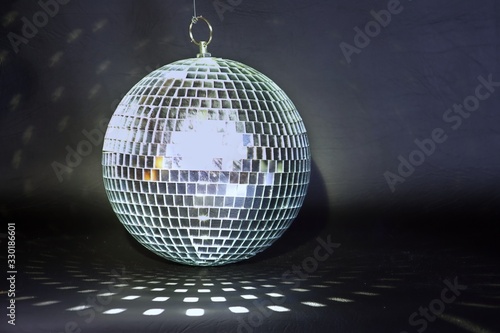 Mirror ball against a black background.  The mirror ball is reflecting a geometric pattern on the dark foreground. Light is reflected off the mirror ball.