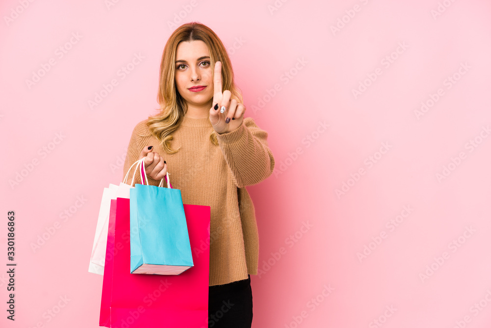 Young blonde woman holding shopping bags isolated showing number one with finger.