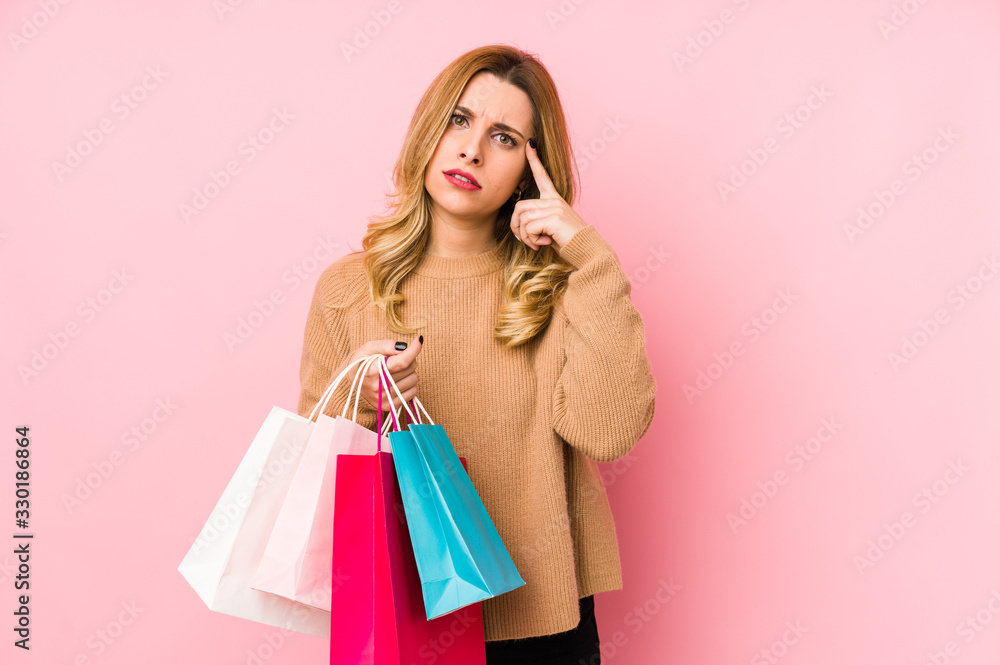 Young blonde woman holding shopping bags isolated showing a disappointment gesture with forefinger.