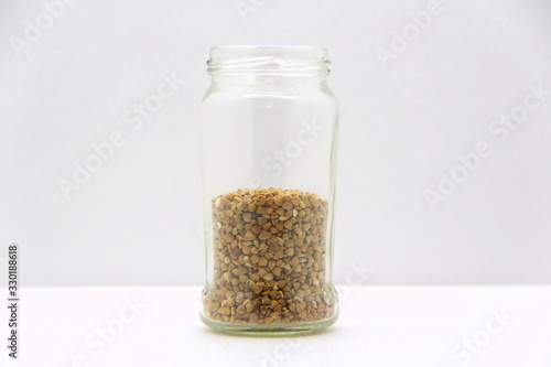 Glass jar with buckwheat on a white background, side view.