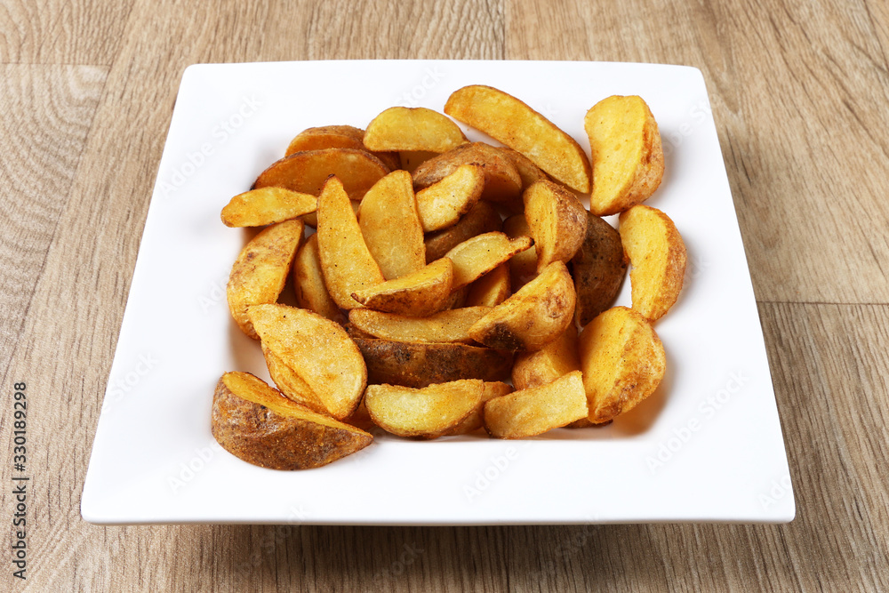 Potato wedges in a white square plate on wooden background Potato wedges in a white square plate on wooden background