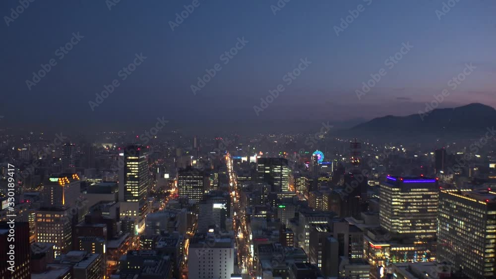 SAPPORO, HOKKAIDO, JAPAN - FEB 2020 : Aerial high angle sunrise view of cityscape of Sapporo city. View of buildings and street traffic around Susukino downtown area. Time lapse shot night to morning.
